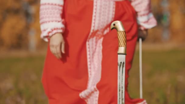 Feisty kvinna i röd lång nationell klänning tar ett svärd och sätta dem kors och tvärs — Stockvideo