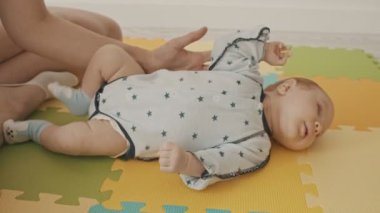 Minik bebek paspasın üzerinde sürünüyor ve annesi onu tutuyor.