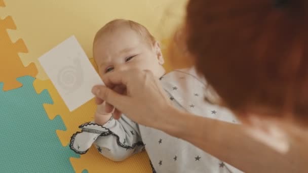 Mãe fazendo exercícios com seu bebê - fazendo-o assistir e seguir um pedaço de papel com um desenho com os olhos — Vídeo de Stock