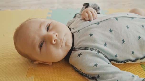Mały chłopiec leżący na plecach na pastelowej macie i patrzący w kamerę — Wideo stockowe