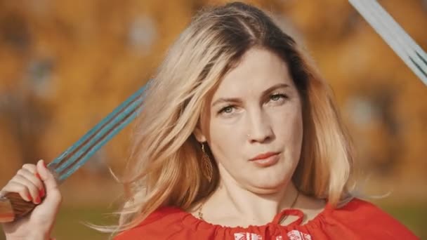 Приваблива жінка в червоному одязі, що стоїть на полі з мечами за її головою — стокове відео
