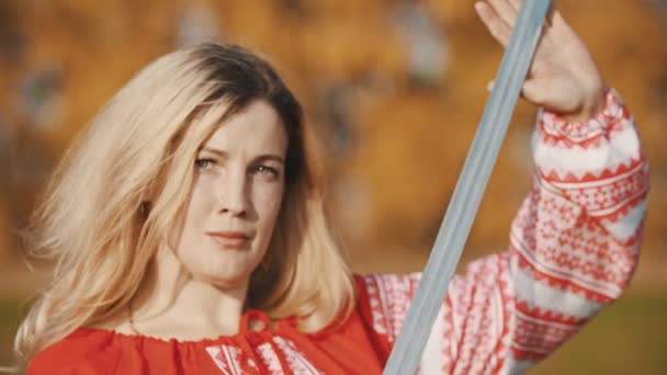 Злая женщина в красной одежде стоит на поле и позирует с мечом — стоковое видео