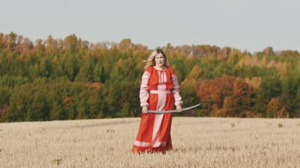 Νευρική γυναίκα με κόκκινα ρούχα στέκεται στο γήπεδο και ποζάρει με καμπυλωτό σπαθί — Αρχείο Βίντεο