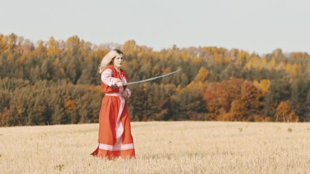 Zadziorna kobieta w czerwonej sukience trening na boisku - szermierka z zakrzywionym mieczem — Wideo stockowe