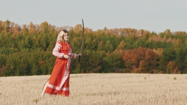 Feisty Frau im roten Kleid beim Training auf dem Feld - trainiert mit einem Schwert und wirft es hoch