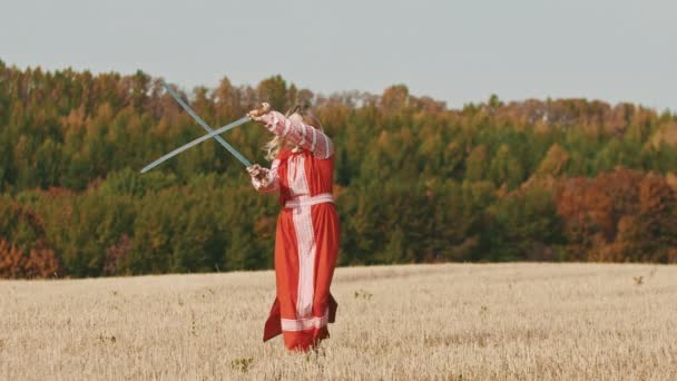 Feisty Frau im roten Kleid beim Training auf dem Feld - trainiert mit zwei gebogenen Schwertern und dreht sie