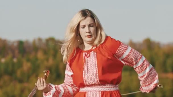 Ритуальна доросла жінка в червоній сукні, що обертає мечі на полі — стокове відео