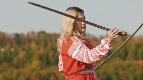 Vurige volwassen vrouw in rode jurk trainen van haar vaardigheden - roteren haar zwaarden op het veld — Stockvideo