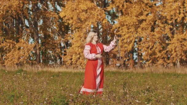 Злая женщина в красном национальном платье вращает меч вокруг себя и бросает его — стоковое видео