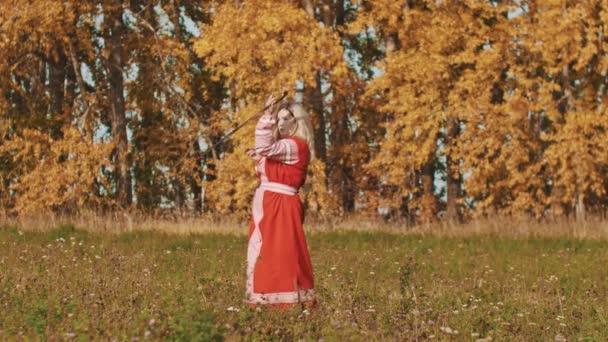 Mulher loira em vestido nacional vermelho girando uma espada em torno de si mesma — Vídeo de Stock