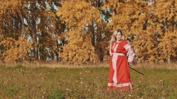 Middeleeuws concept - vrouw in rode nationale lange jurk die een zwaard om zich heen draait — Stockvideo