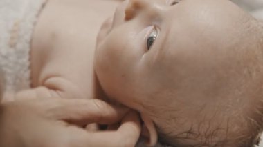 Küçük bir bebek yatakta yatıyor ve ailesi kulak temizliyor kulak pamuklarıyla.