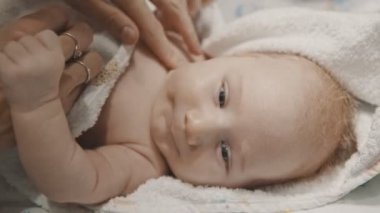 Küçük bir bebek yatakta yatıyor ve annesi uyumadan önce yüzünü siliyor.
