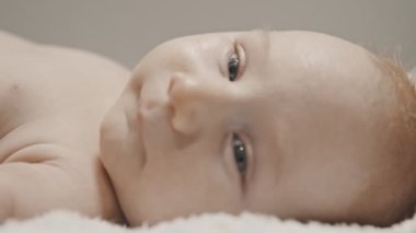 Küçük bir bebek yatakta yatıyor ve annesi onu yan tarafa çeviriyor.