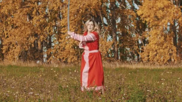 Mittelalterliches Konzept - Frau in rotem Nationalkleid schwingt meisterhaft Schwerter - wirft einen hoch und fängt mit der anderen Hand — Stockvideo