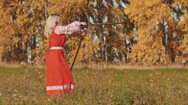 Mittelalterliches Konzept - Frau in roter Tracht trainiert auf dem Feld - schwingt meisterhaft Schwerter - dreht sie herum — Stockvideo