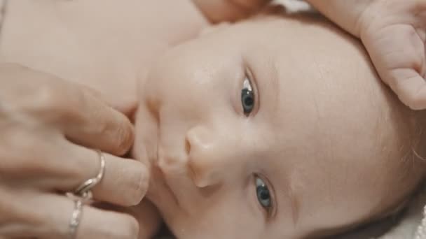 Un petit bébé aux yeux bleus couché au lit et sa mère appliquant de la crème dans son cou — Video