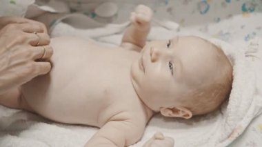 Küçük bir bebek yatakta yatıyor ve annesi göbeğini bantlıyor.