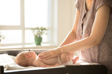Anne, elleri küçük bebeğinin üzerinde bir yatakta yatıyor.
