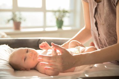 Anne küçük bebeğiyle ilgileniyor. Yatakta yatıyor.