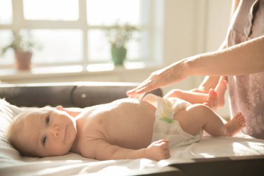 Anne, elleri, gülümseyen bebeğinin üzerinde yatakta yatarken.