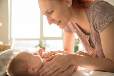 Gülümseyen şefkatli anne küçük bebeğine bakıyor.