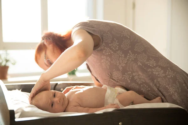 Mom takes care of her small baby lying on a bed — Stock Photo, Image