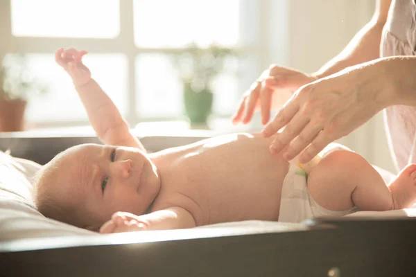 Rusteloze baby liggend op het bed en zijn moeder op het punt om zijn luier te verschonen — Stockfoto