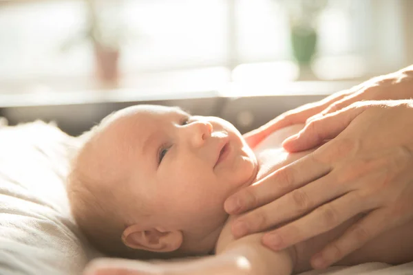 Mammas händer på hennes leende baby liggande på en säng — Stockfoto