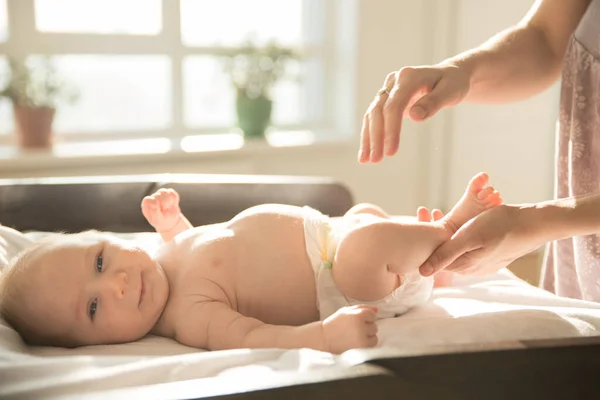 Moeder masseren benen van haar kleine baby liggend op een bed — Stockfoto