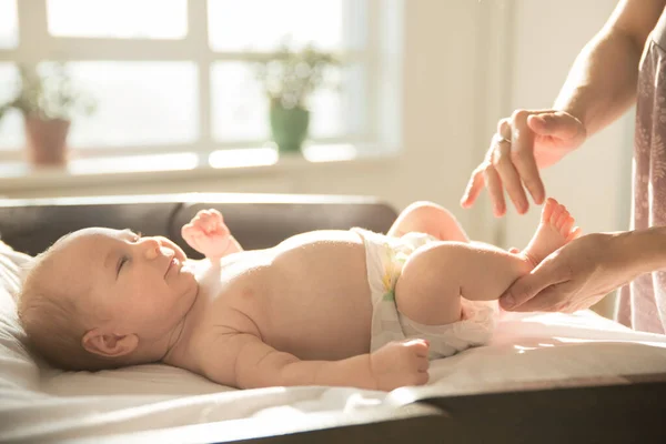 Mãe massagem pernas de seu pequeno bebê sorridente deitado em uma cama — Fotografia de Stock