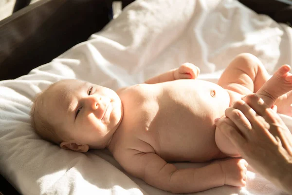 Een kleine lachende baby op een bed op witte lakens — Stockfoto
