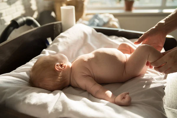 Um bebezinho deitado em uma cama em lençóis brancos e seu pai segurando suas pernas — Fotografia de Stock