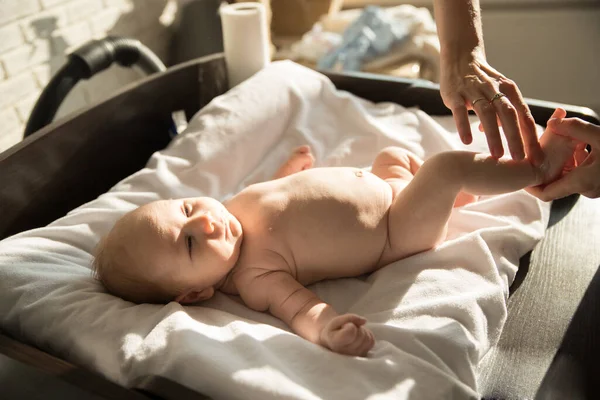 En liten bebis som ligger på en säng på vita lakan och hans förälder masserar hans ben — Stockfoto