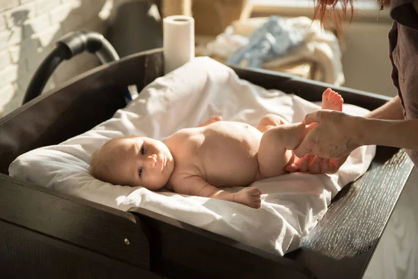 En bebis som ligger på en säng på vita lakan och hans förälder som håller i benen — Stockfoto