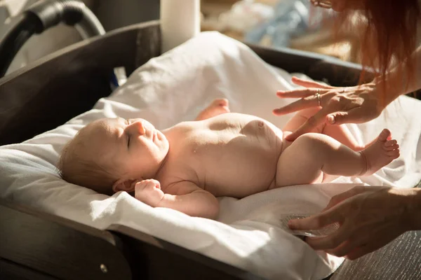 Ett litet barn som ligger på en säng på vita lakan och hans förälder håller sin kropp — Stockfoto