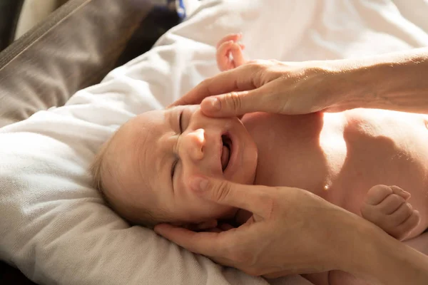 一个哭哭啼啼的小宝宝躺在床上，他的父母在按摩他的脸 — 图库照片