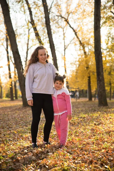 Dos hermanas de pie en el parque de otoño abrazándose — Foto de Stock