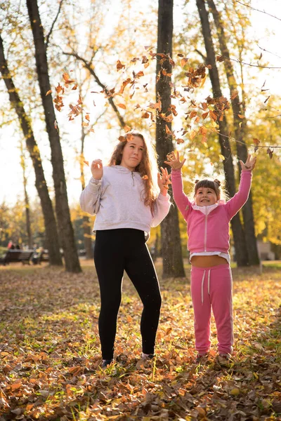 Mamá e hija vomitando hojas muertas en el parque de otoño — Foto de Stock