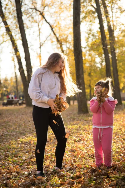 Hermanas sosteniendo hojas de naranja en el parque de otoño — Foto de Stock