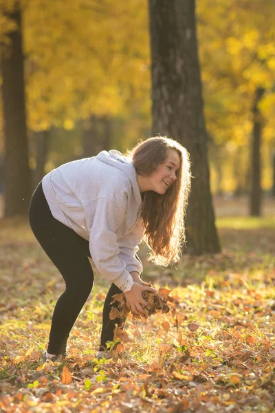 Mladá žena drží žluté listy v podzimním parku — Stock fotografie