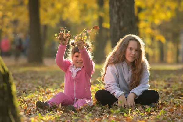 Dos hermanas sentadas en el suelo en el parque de otoño — Foto de Stock