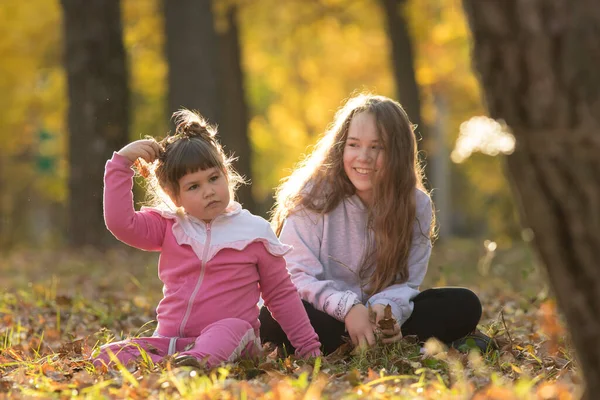 Hermanas mayores y pequeñas sentadas en el suelo en el parque de otoño — Foto de Stock