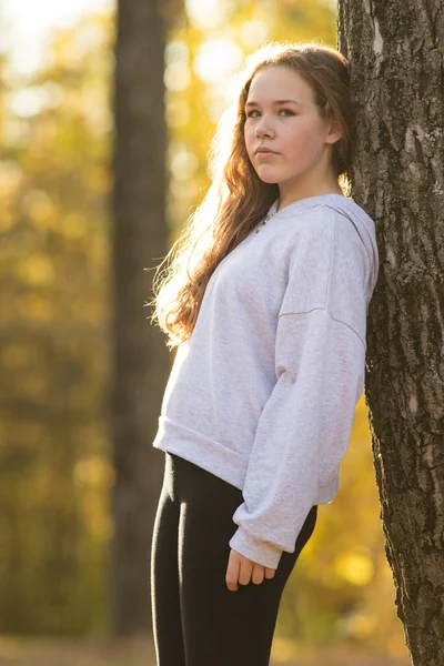 Fiatal nő tini fehér kapucnis áll a fa mellett az őszi parkban — Stock Fotó