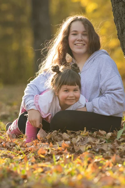 Dos hermanas sonrientes sentadas en el suelo en el parque de otoño — Foto de Stock