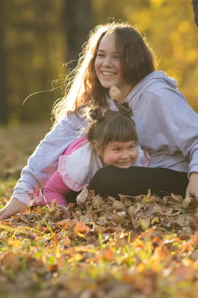 Dos hermanas sonrientes sentadas en el suelo en el parque amarillo de otoño — Foto de Stock