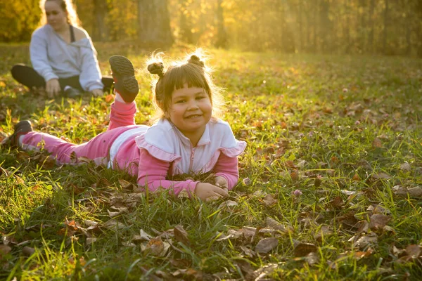 Dos hermanas en el parque de otoño: una niña pequeña tirada en el suelo — Foto de Stock