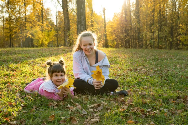Dos hermanas en el parque de otoño: una niña tendida en el suelo y otra sentada junto a ella — Foto de Stock