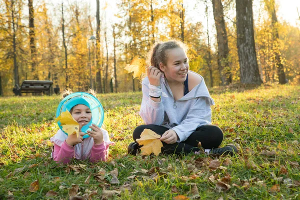 Dos hermanas en el parque de otoño: una niña acostada en el suelo y otra sentada junto a ella — Foto de Stock