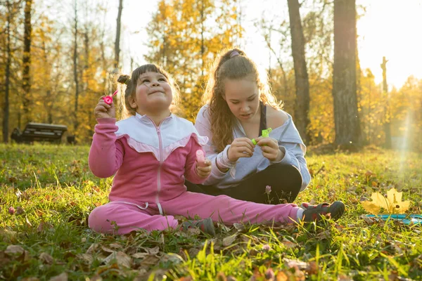 Dos hermanas en el parque de otoño: una niña sentada en el suelo y otra sentada junto a ella — Foto de Stock